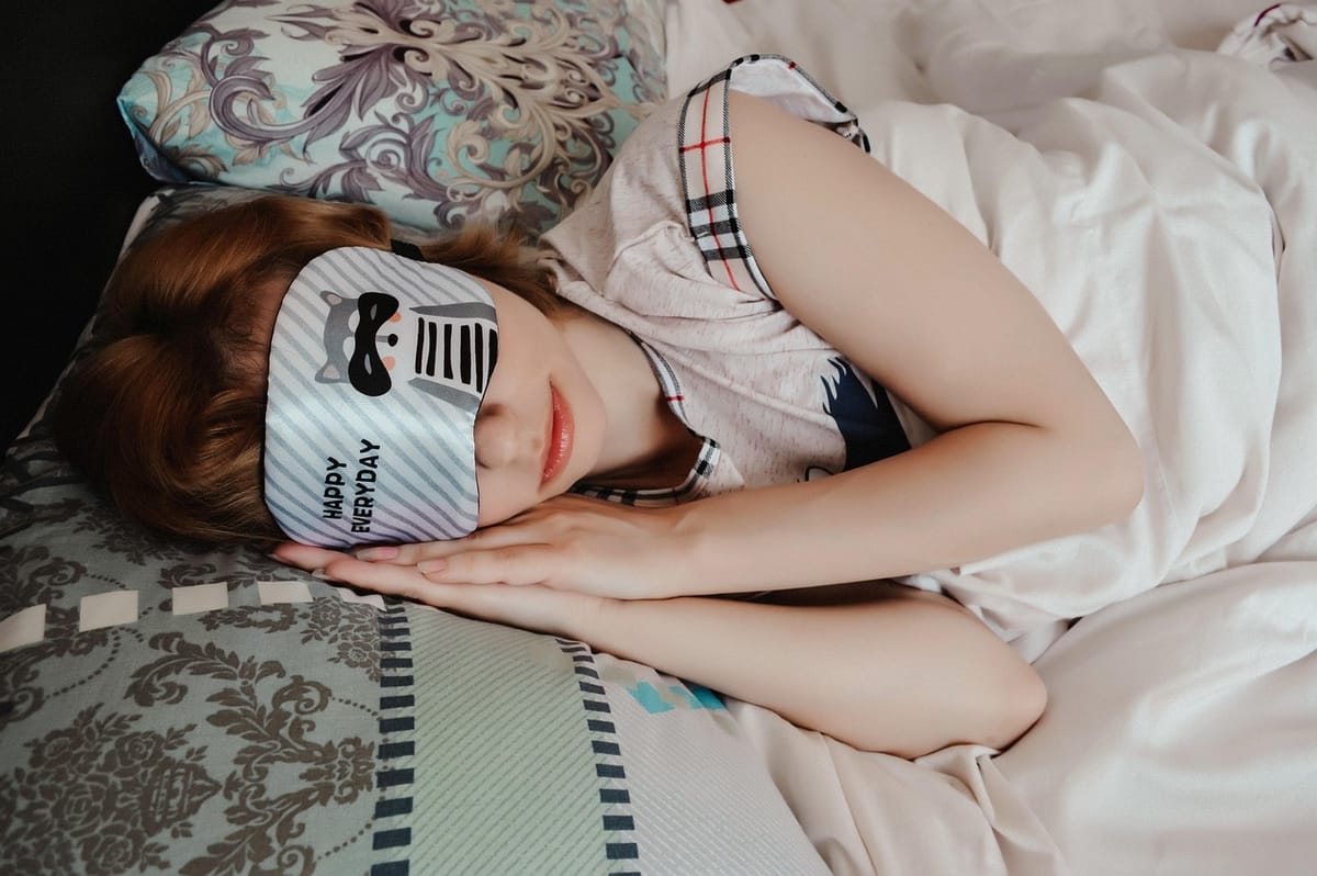 A person lying in bed, sleeping with a sleep mask in bed.